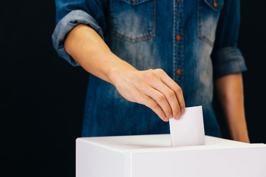 Front view of person holding ballot paper casting vote at a polling station for election vote in black background